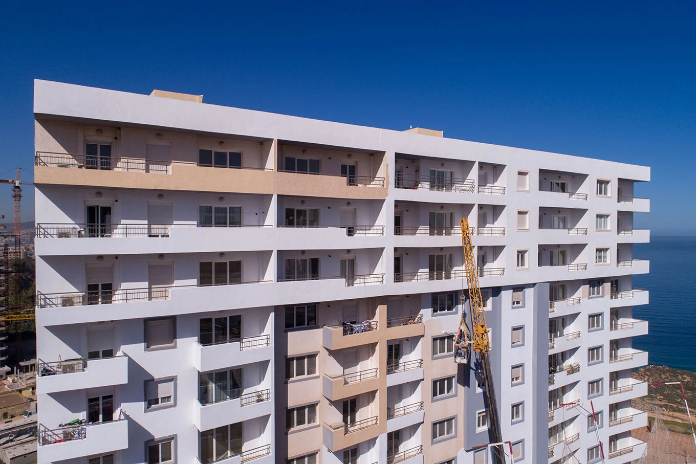 un immeuble blanc avec plusieurs balcons amenagé avec des fenetres pvc en double vitrage isolant et des volets en lames pvc dans un chantier a oran